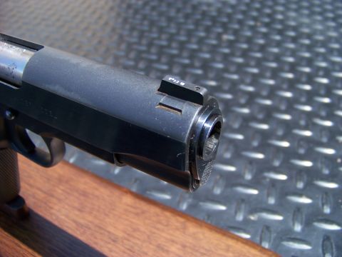 1995 Mercury Grand Marquis - A close-up shot of the muzzle end of a dark-colored handgun. The gun is resting on a wooden surface, with a diamond plate textured backgrou…