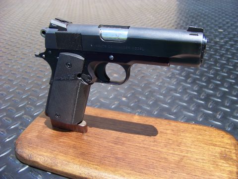 1995 Mercury Grand Marquis - A black semi-automatic handgun is displayed on a wooden base. The handgun is resting on a textured metal surface.