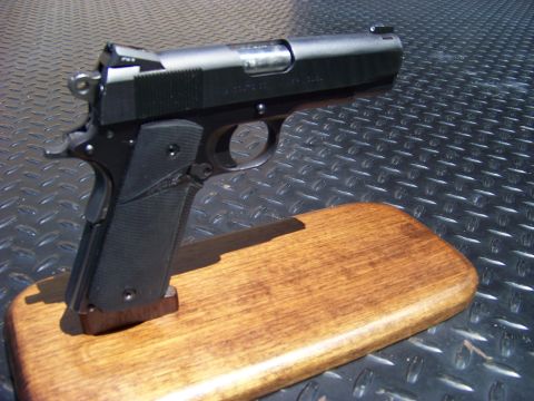 1995 Mercury Grand Marquis - A close-up, angled shot of a black semi-automatic handgun resting on a wooden display stand. The handgun is positioned on a textured metal…