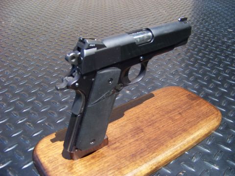 1995 Mercury Grand Marquis - A black semi-automatic pistol rests on a wooden display stand against a diamond plate background.
