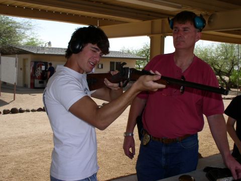 1990 Ford Bronco - A young man practices aiming a rifle at an outdoor shooting range, with an instructor observing.