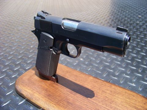 1995 Mercury Grand Marquis - A black semi-automatic pistol with textured grips rests on a wooden stand. The pistol is positioned against a background of diamond plate m…