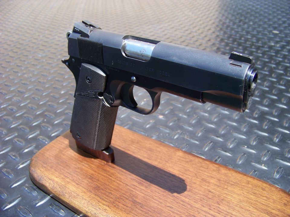 Black semi-automatic pistol on a wooden stand against a diamond plate background.