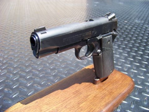 1995 Mercury Grand Marquis - A black semi-automatic pistol is displayed on a wooden stand against a textured metal background.