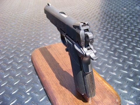 1995 Mercury Grand Marquis - A close-up, angled view of a black semi-automatic handgun resting on a wooden surface. The background is a textured metal surface.