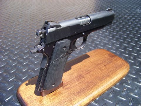 1995 Mercury Grand Marquis - A black semi-automatic pistol is displayed on a wooden base against a textured metal background.