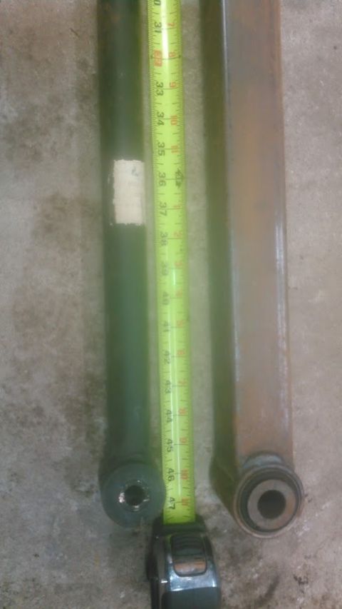 1992 Ford Bronco - A measuring tape is placed alongside two automotive control arms, one dark green and the other rusty brown. The tape measure shows a length…