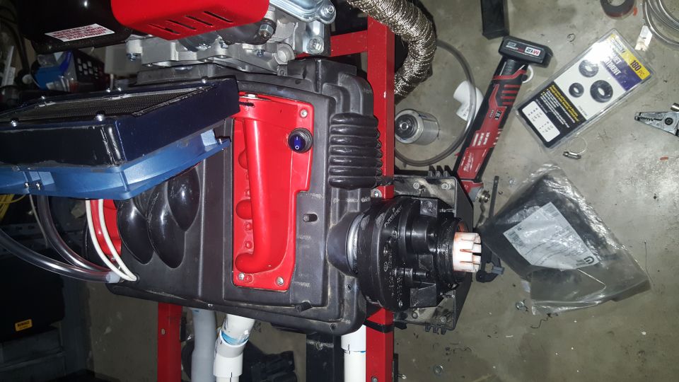 Close-up of a mechanical device with red and black components, tubes, and wires on a concrete floor.