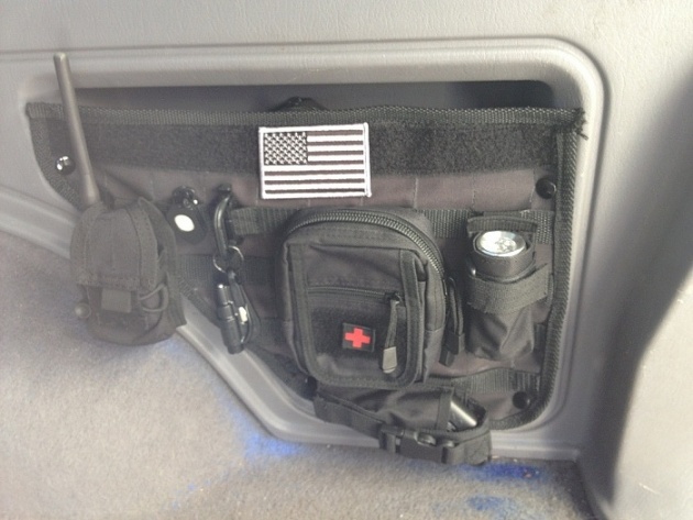 Black MOLLE organizer attached to vehicle interior wall with American flag patch, medical pouch, flashlight, and radio