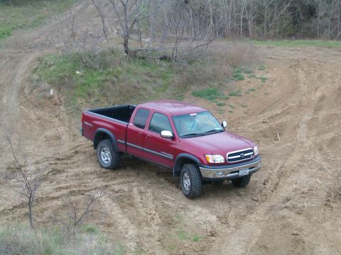 1996 Ford Bronco - This red Toyota Tundra pickup truck is driving on a dirt road with trees in the background.