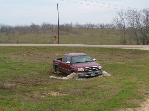 1996 Ford Bronco - Red Toyota Tundra stuck in mud off the side of a road.
