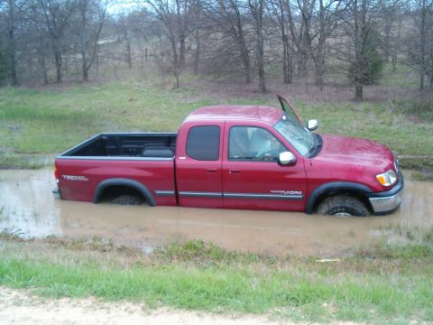1996 Ford Bronco - This red Toyota Tundra is stuck in a muddy area with the driver's door open.