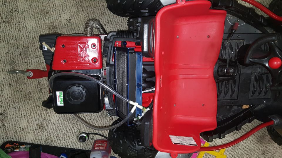 Red plastic toy vehicle engine with black fuel tank and silver exhaust pipe, viewed from above
