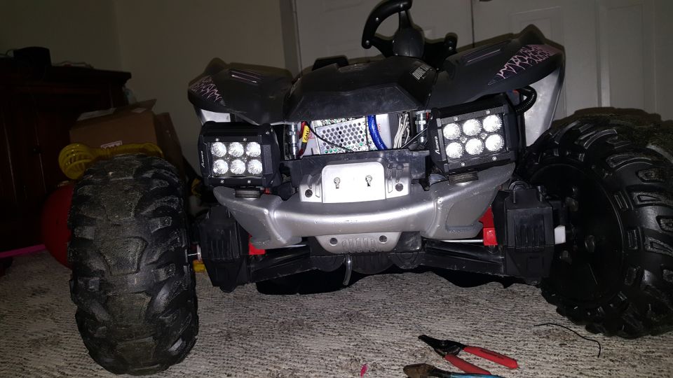 Toy ATV with large tires, aftermarket LED light bars, and exposed wiring