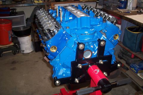 1995 Ford Bronco - A blue V8 engine is mounted on a red engine stand in a workshop.