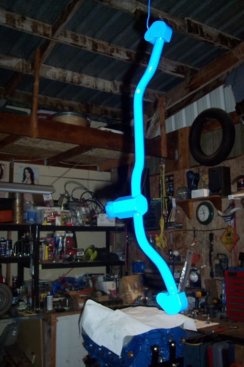 1995 Ford Bronco - A bright blue painted suspension component hangs suspended in a cluttered garage setting.