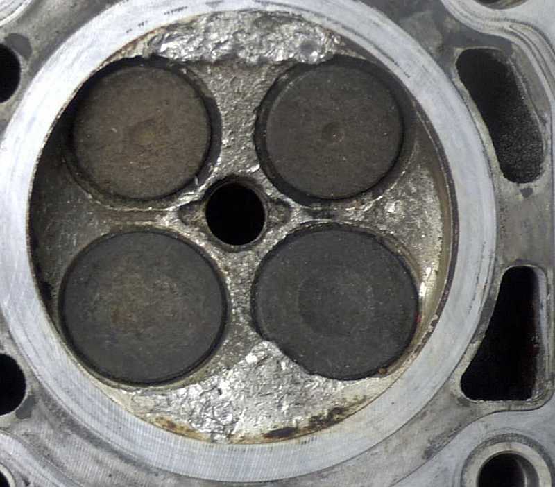 Close-up of a cylinder head with four valves and a central spark plug hole.