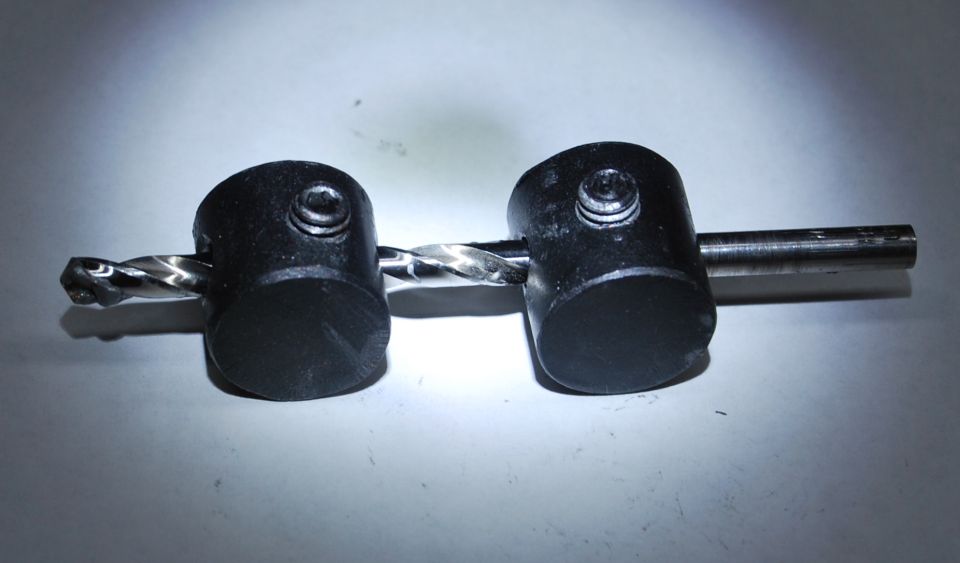 Drill bit passing through two black cylindrical objects with screws.