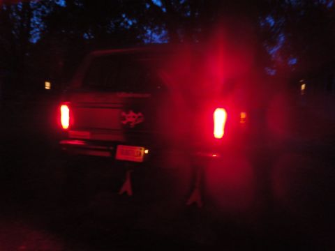 1978 Ford Bronco - The rear of a dark-colored SUV is shown at night, with its red taillights illuminated. A skull and crossbones sticker is visible on the tai…