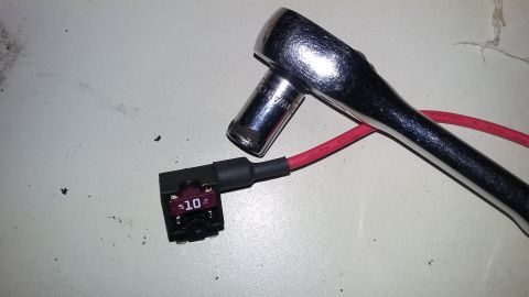 2000 Pontiac Grand Prix - A close-up shot shows a 10-amp fuse tap with a red wire connected to it, and a socket wrench is positioned over the fuse tap. The items are…
