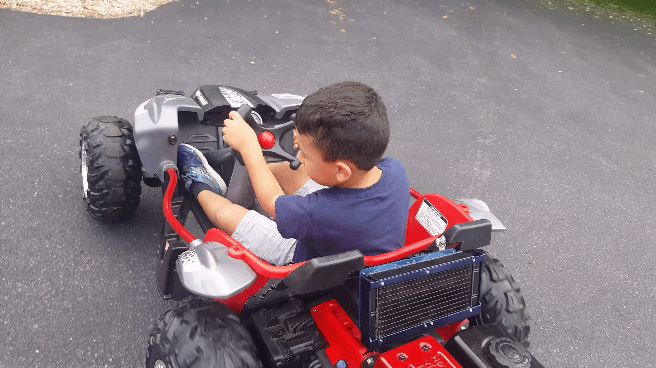 Young boy in a blue t-shirt and grey shorts driving a red and silver toy ATV.