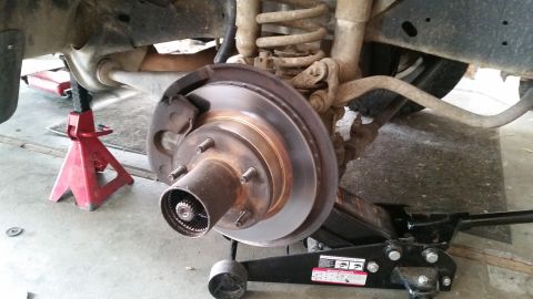 1985 Ford Bronco - A close-up view of a vehicle's front brake rotor and hub assembly, supported by a red jack stand and a black hydraulic floor jack. The vehi…