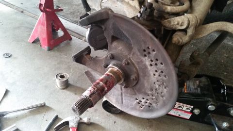 1985 Ford Bronco - A close-up view of a vehicle's front suspension and braking system, including a brake rotor with numerous small holes, a greased spindle, a…