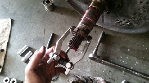 1985 Ford Bronco - A hand uses a gear puller to remove a greased splined shaft from a larger component, likely part of a vehicle's drivetrain. Several socket…