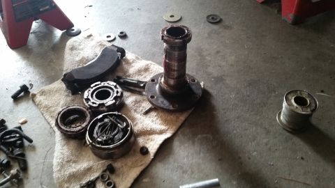 1985 Ford Bronco - A disassembled wheel hub assembly and brake components are laid out on a towel on a concrete floor. A red jack stand is visible in the back…