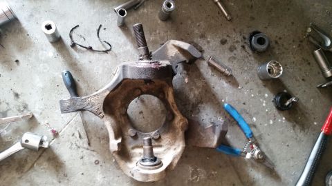 1985 Ford Bronco - A collection of automotive parts and tools are laid out on a concrete surface. The main part appears to be a vehicle's steering knuckle wit…