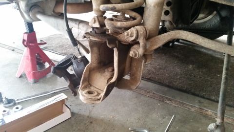 1985 Ford Bronco - The underside of a vehicle is shown, with the suspension components disassembled and supported by jack stands. Tools and parts are laid out…