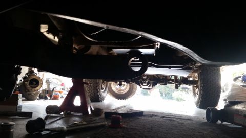 1985 Ford Bronco - The underside of a vehicle is shown, with the suspension and drivetrain components visible. The vehicle appears to be raised on jack stands…