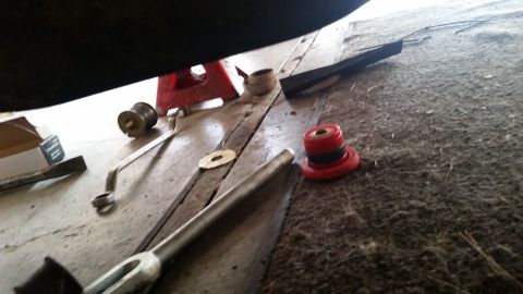 1985 Ford Bronco - A red and black polyurethane bushing sits on a carpeted surface next to a metal wrench and a washer. The underside of a vehicle, possibly a…