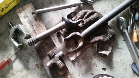 1985 Ford Bronco - A collection of automotive parts, including a driveshaft, U-joints, and a ball joint separator tool, are laid out on a concrete floor next…