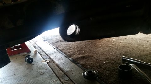 1985 Ford Bronco - A close-up, low-angle shot of the underside of a vehicle's frame, showing a large circular opening. Tools and suspension parts are visible…