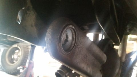 1985 Ford Bronco - Close-up view of a rusty metal suspension component, likely a control arm or linkage, attached to the undercarriage of a vehicle. A tire an…