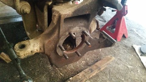 1985 Ford Bronco - A close-up view of a rusty, disassembled vehicle suspension component, likely a spindle or knuckle, with several studs protruding. A red ja…