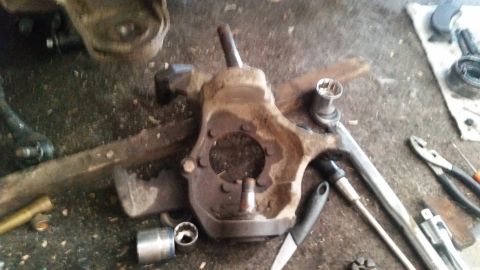 1985 Ford Bronco - A disassembled vehicle suspension component, likely a steering knuckle, is laid out on a workbench with various tools including a socket wr…