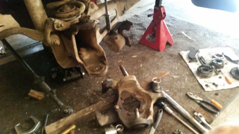 1985 Ford Bronco - This image shows a disassembled vehicle suspension system, likely from a 1985 Ford Bronco, with various parts laid out on the floor. Tools…