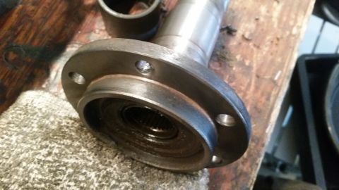 1985 Ford Bronco - A close-up view of a splined hub with a flange, likely a part from a vehicle's drivetrain, resting on a textured surface next to a wooden w…