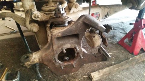 1985 Ford Bronco - A close-up view of a rusty, disassembled front suspension component, likely from a 1980s era 4x4 vehicle, is shown supported by jack stands.