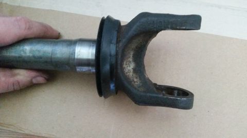 1985 Ford Bronco - A close-up view of a U-joint yoke attached to a metal shaft, held by a hand. The yoke is dark gray and shows signs of rust and wear.