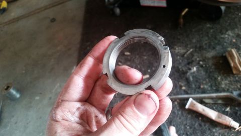 1985 Ford Bronco - A person's dirty hand holds a damaged, threaded metal nut with notches around its outer edge. The background shows a workshop floor with va…