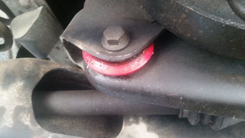 1985 Ford Bronco - A close-up view shows a red polyurethane bushing installed on a vehicle's suspension component, secured by a bolt.