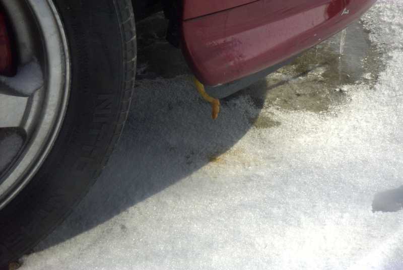 Close-up of a red car's lower door and tire in the snow. A yellow object is visible under the door