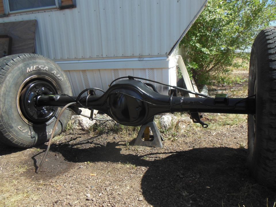 Freshly painted black solid rear axle housing on jack stands outdoors near tires