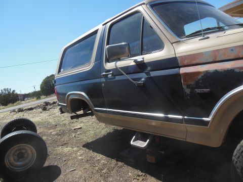 1984 Ford Bronco - The side view of a two-tone brown and dark blue Ford Bronco is shown outdoors on a sunny day. The vehicle is missing a rear wheel and is su…