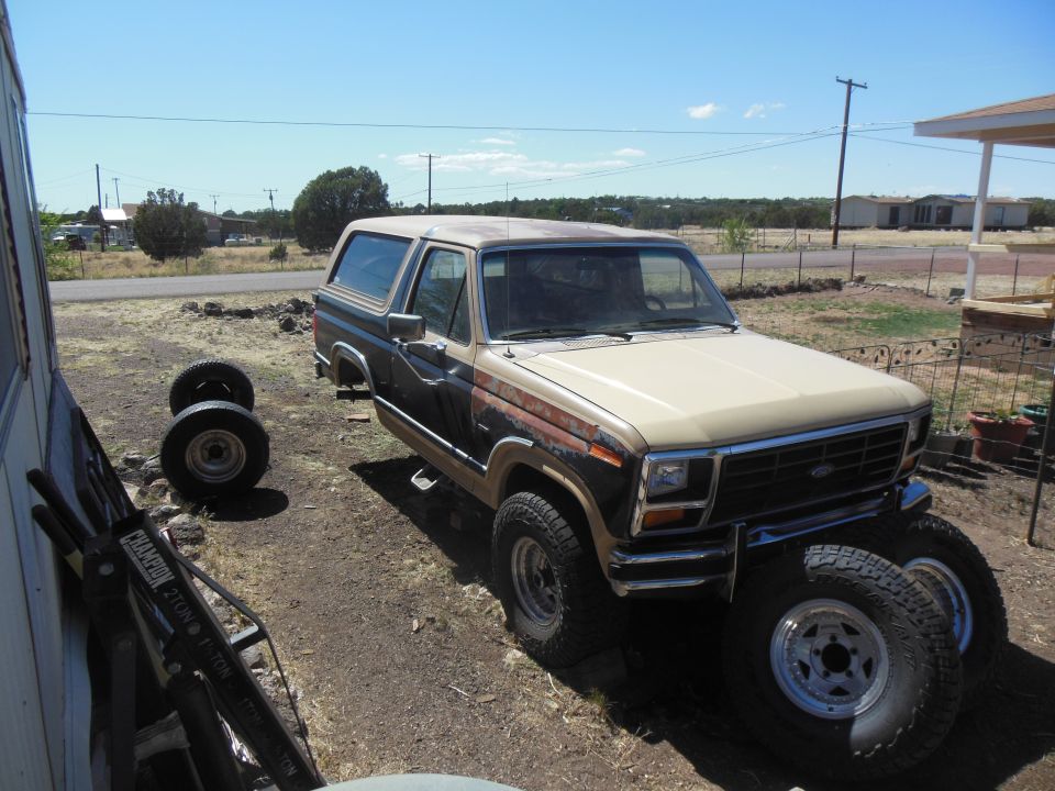 1980s Ford Bronco with spare tires in a dirt lot.