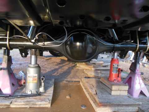 1984 Ford Bronco - The underside of a vehicle's rear axle assembly is supported by two bottle jacks and two jack stands. The axle housing and suspension compo…