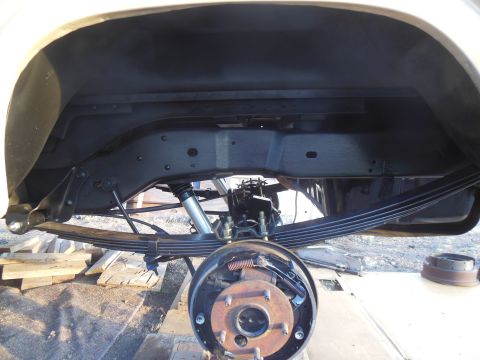 1984 Ford Bronco - The underside of a vehicle's rear suspension is shown, featuring leaf springs, a shock absorber, and a brake drum assembly. The frame and w…